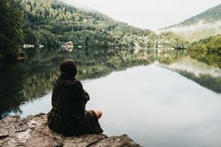 Woman sitting with blanket near lake and mountains