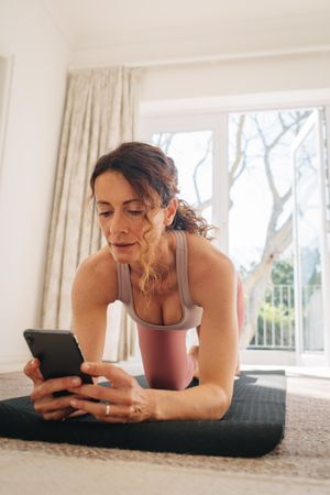 Woman using her smart phone to find workout tutorials online with exercising at home