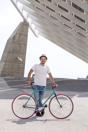 Male with bicycle standing under modern building, vertical
