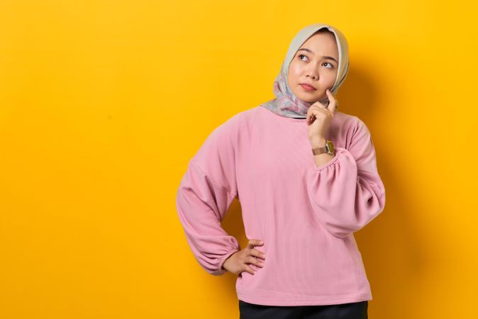 Muslim woman in headscarf contemplating something with finger on cheek