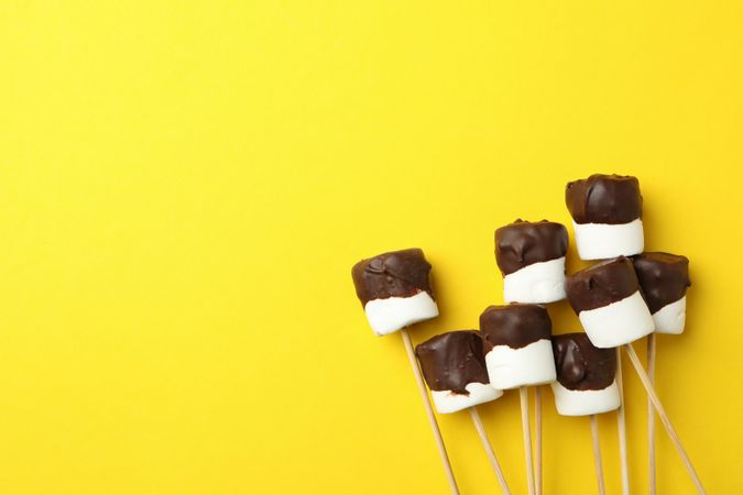 Marshmallows in chocolate on yellow background, space for text