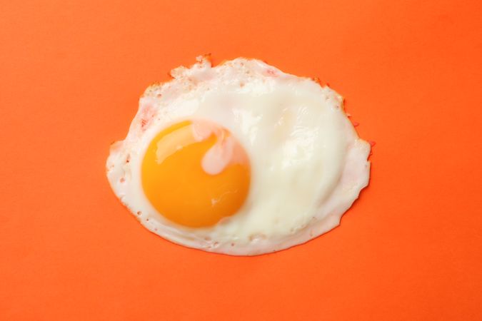 Top view of fried egg, sunny side up on orange background