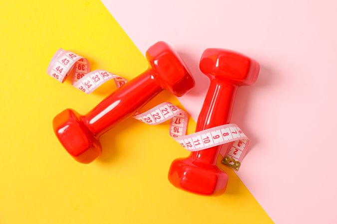 Dumbbells and measuring tape on two tone background, copy space