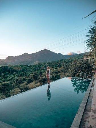 Woman standing at edge of swimming pool near mountains