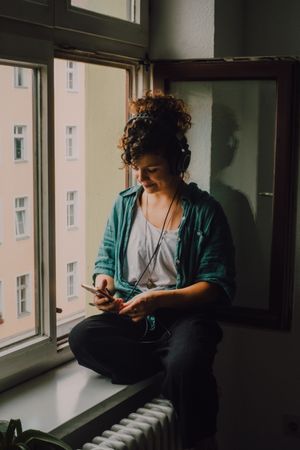 Cheerful woman in headphones using smartphone at home