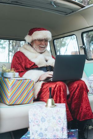 Santa Claus working at laptop in van