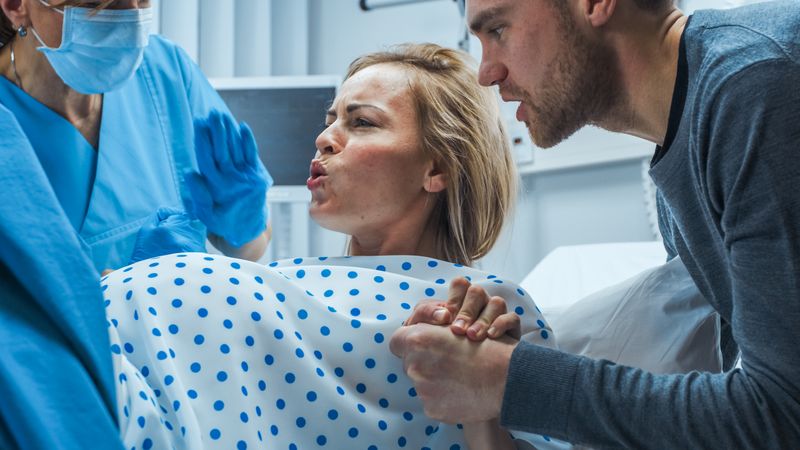 In the Hospital, Close-up on a Woman in Labor Pushing Hard to Give Birth, Obstetricians Assisting, Spouse Holds Her Hand