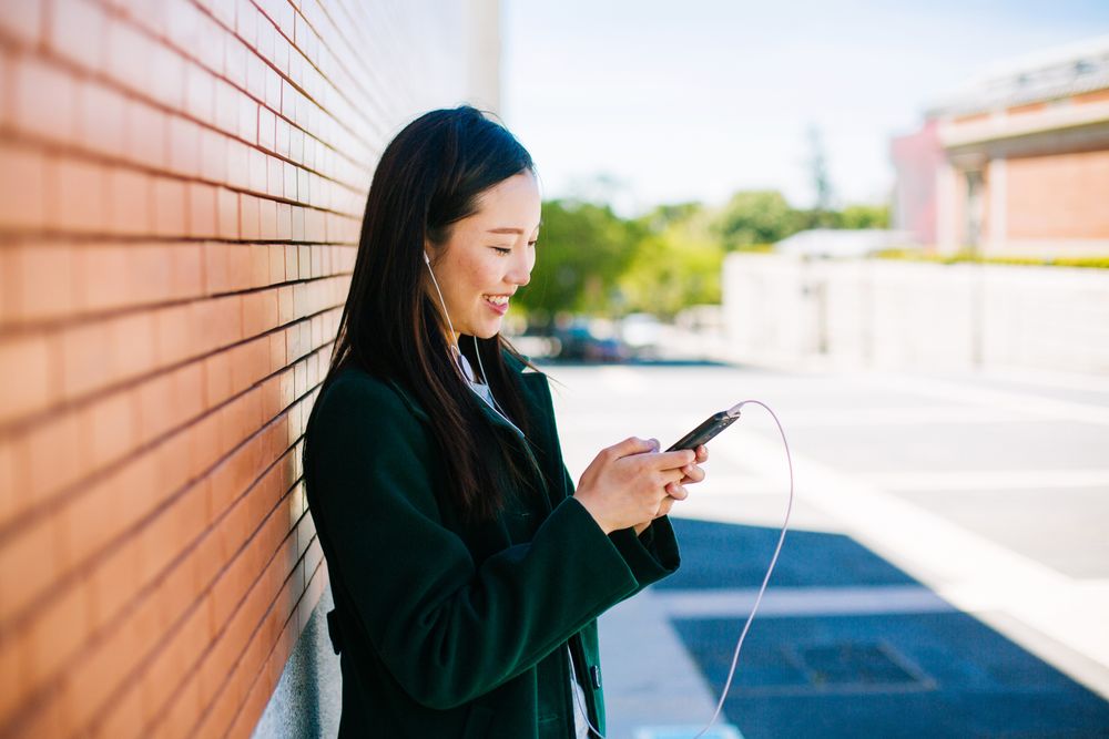Asian female listening to music near brick wall
