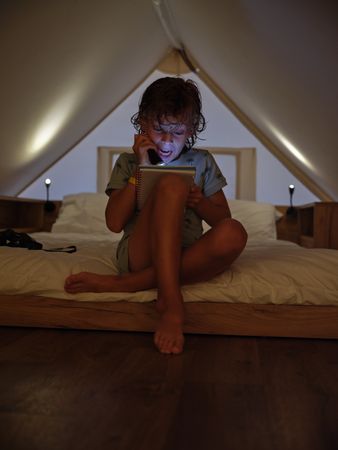 Astonished boy reading book with flashlight