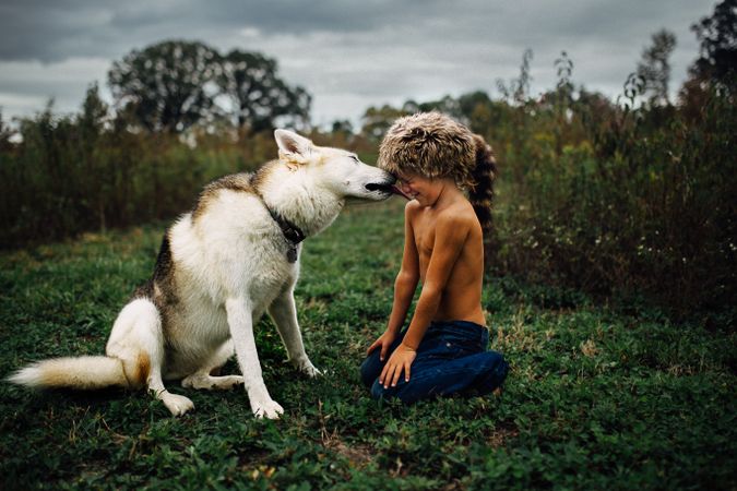 Czechoslovakian Wolfdog cuddling with young boy wearing a raccoon hat in nature
