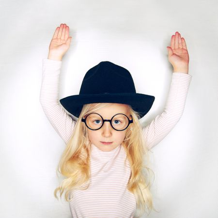 Serious blonde girl with arms up in hat and glasses