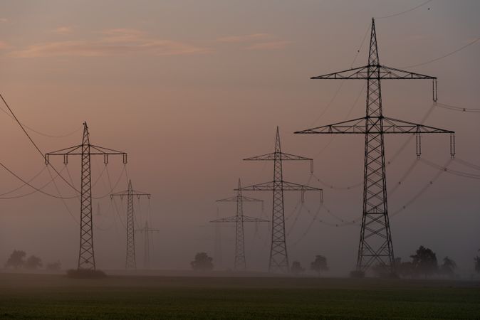 Electricity pylons on agricultural fields at golden on a foggy morning