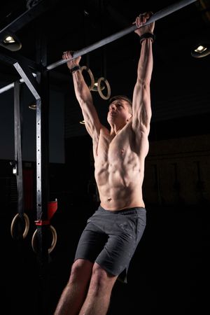 Muscular sportsman doing pull ups on bar
