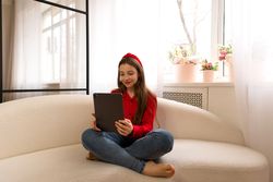 Teen girl using tablet while sitting cross-legged on sofa.