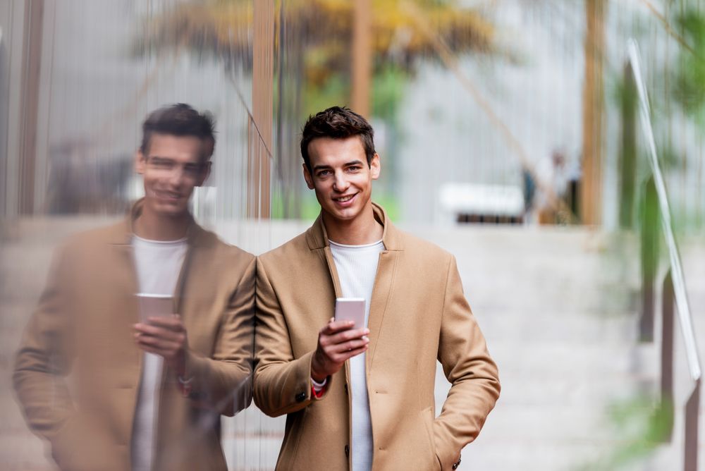 Man standing against reflective wall and looking up from phone