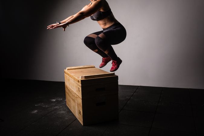 Woman jumping on wooden box in gym