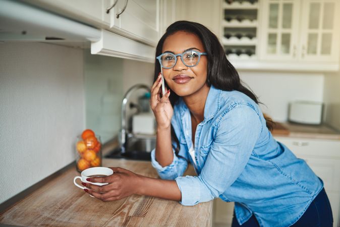 Woman taking phone call while leaning over kitchen counter