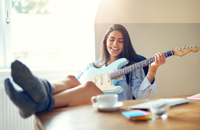 Woman having fun and smiling while playing guitar at her desk