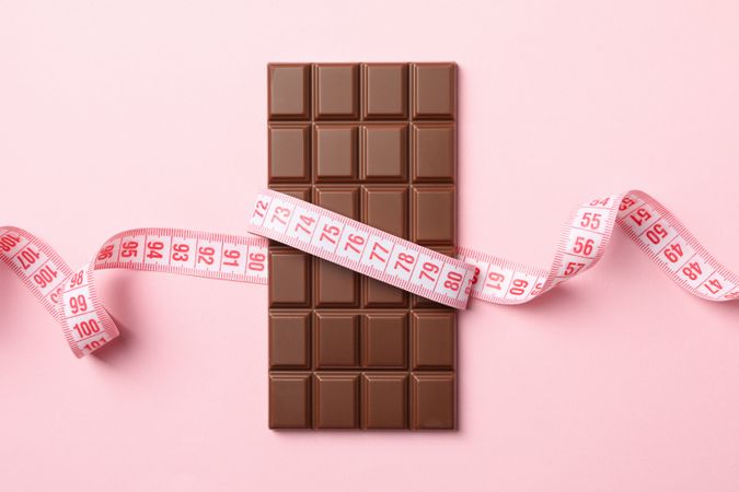 Measuring tape and chocolate bar on pink background