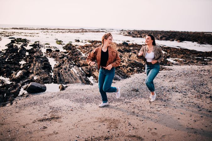 Two trendy young women running playfully along the beach