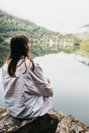 Woman sitting on rock near lake and mountains