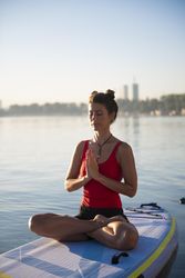 Woman peacefully meditating on paddleboard with her hands together