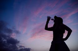 Woman drinking water and sky with clouds at sunset