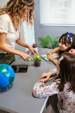 Female teacher showing pansy plant to her happy students in ecology classroom