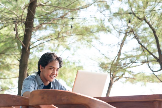 Happy Asian Young businessman work at outdoor with laptop. Concept of remote and freelance work. Young successful man wearing casual blue cloth.