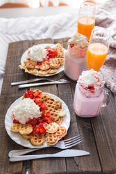 Appetizing waffles with jam and tasty drinks on tray on bed