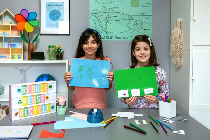 Female students looking at camera and showing drawings with ideas to be more ecological