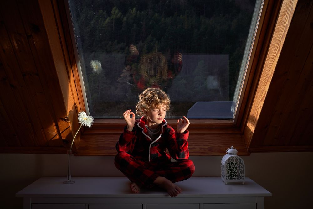 Adorable boy sitting in Lotus pose on chest of drawers