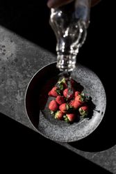 Hand with bottle pouring water on strawberries in plate