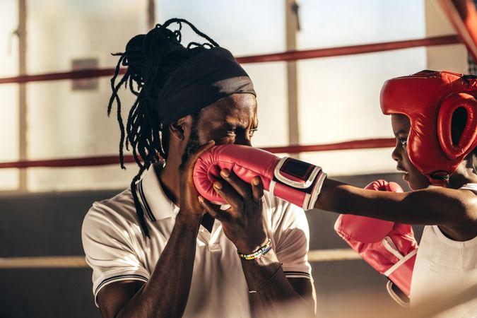 Girl wearing boxing gloves and headgear learning boxing from her coach