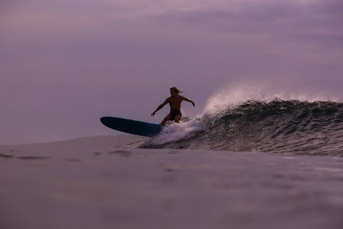 Man on surf board on waving water at sunset