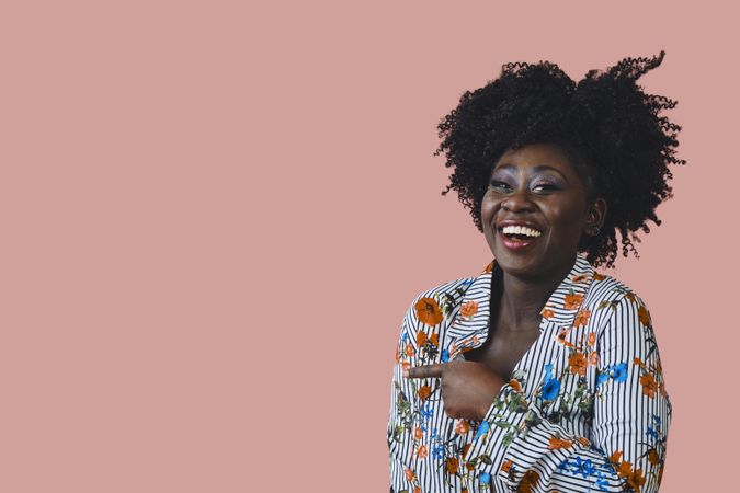 Studio shot of joyful Black woman in floral print shirt pointing at something to the side