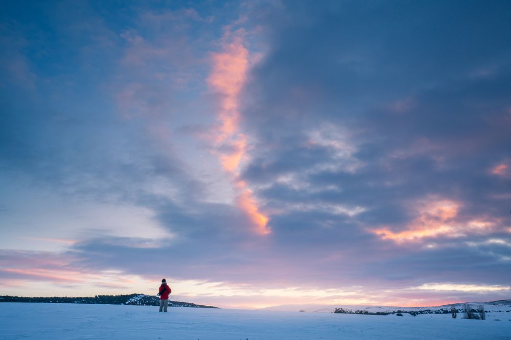 Traveler standing on snow against sunset sky