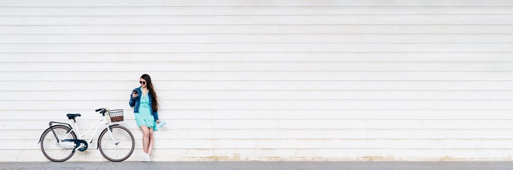 Woman in blue dress leaning on light wall near bicycle