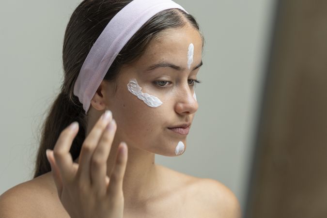 Young woman in profile applying dabs of face cream in a pattern for her beauty routine