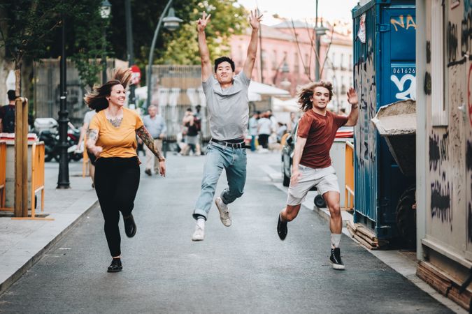Funny multiracial friends having fun and running along city street