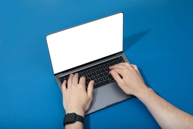 Person on laptop at angle with blank screen in blue room