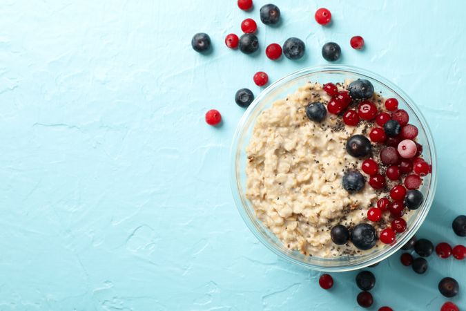 Bowl with oatmeal porridge and fruits on blue background