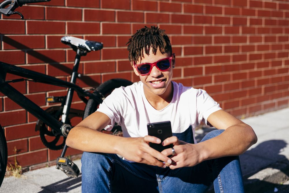 Young happy Black male browsing smartphone near bike