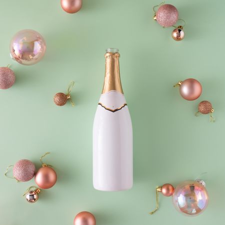 Champagne bottle and Christmas baubles on light green surface