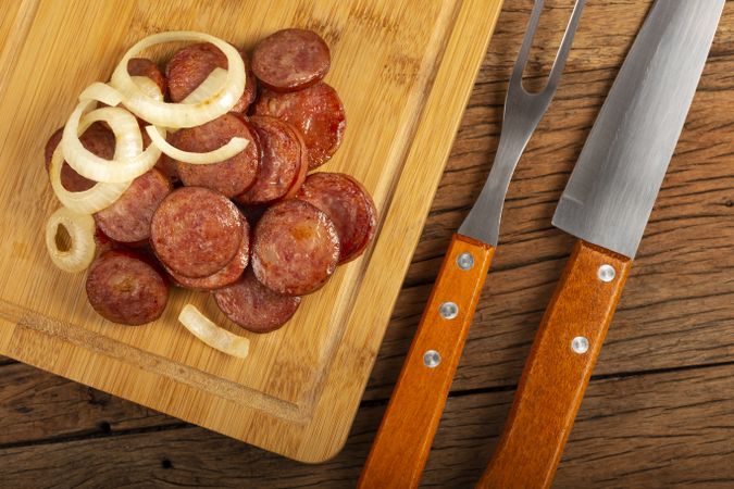 Sliced calabrese sausage with onion on wooden background.