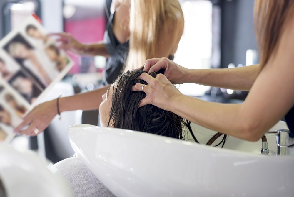 Female client choosing hair style from magazine while having her hair washed