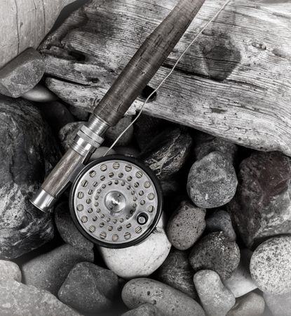 Antique fly fishing outfit on rocks and wood of riverbed