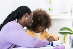 Black father helping daughter with homework on laptop