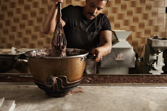 Black male chef using large whisk in steel bowl with melted chocolate
