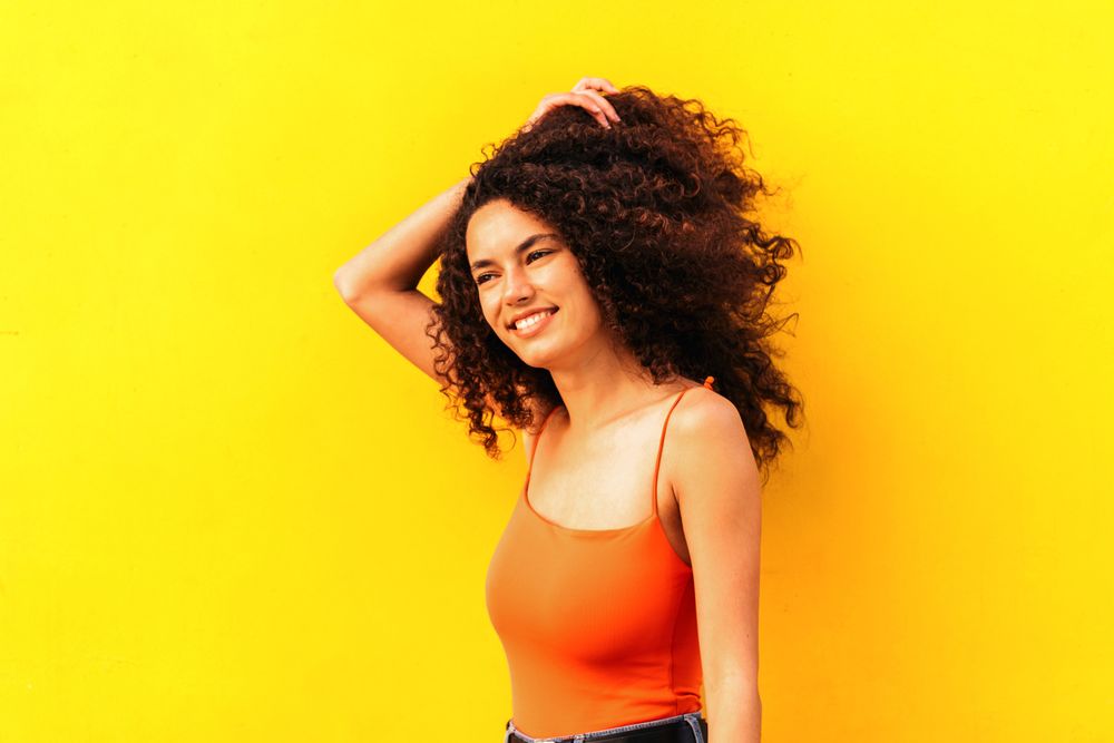 afro latina woman looking aside portrait leaning on a yellow wall